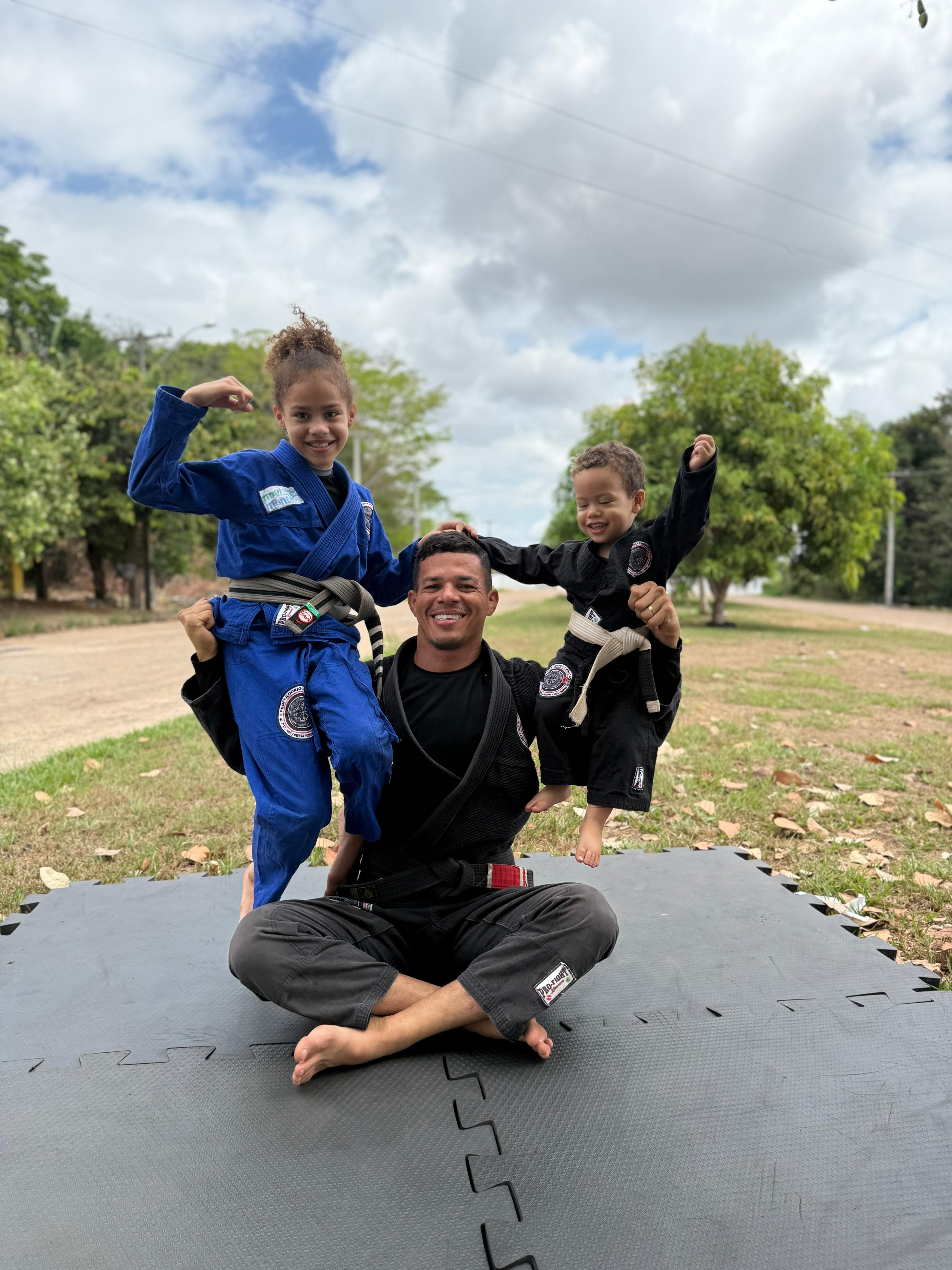 Professor Rodrigo segurando os filhos de kimono no tatame